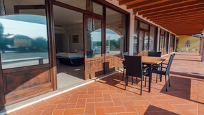 A covered patio area with a wooden table and chairs, large glass doors leading to a bedroom, and a view of the outside. - Lake Harmony Suite - One Bedroom Apartment, Sleeps 4 (Manerba del Garda)