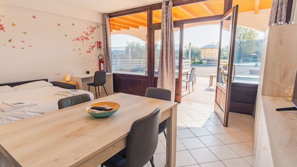 A hotel room with a bed, a desk, a dining table, and a view of the outside. - Lake Harmony Suite - One Bedroom Apartment, Sleeps 4 (Manerba del Garda)