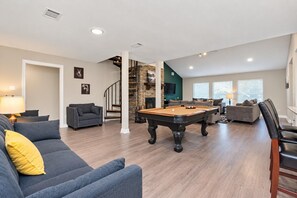 Een ruime woonkamer met een pooltafel, comfortabele zitplaatsen, een trap en een open haard.