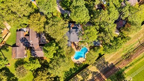 Luchtbeeld van een woonwijk met huizen, een zwembad en omliggend groen.