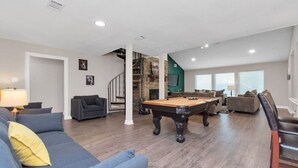 Ein großzügiger Wohnraum mit Billardtisch, Sofas und einer Treppe zu einer oberen Ebene.