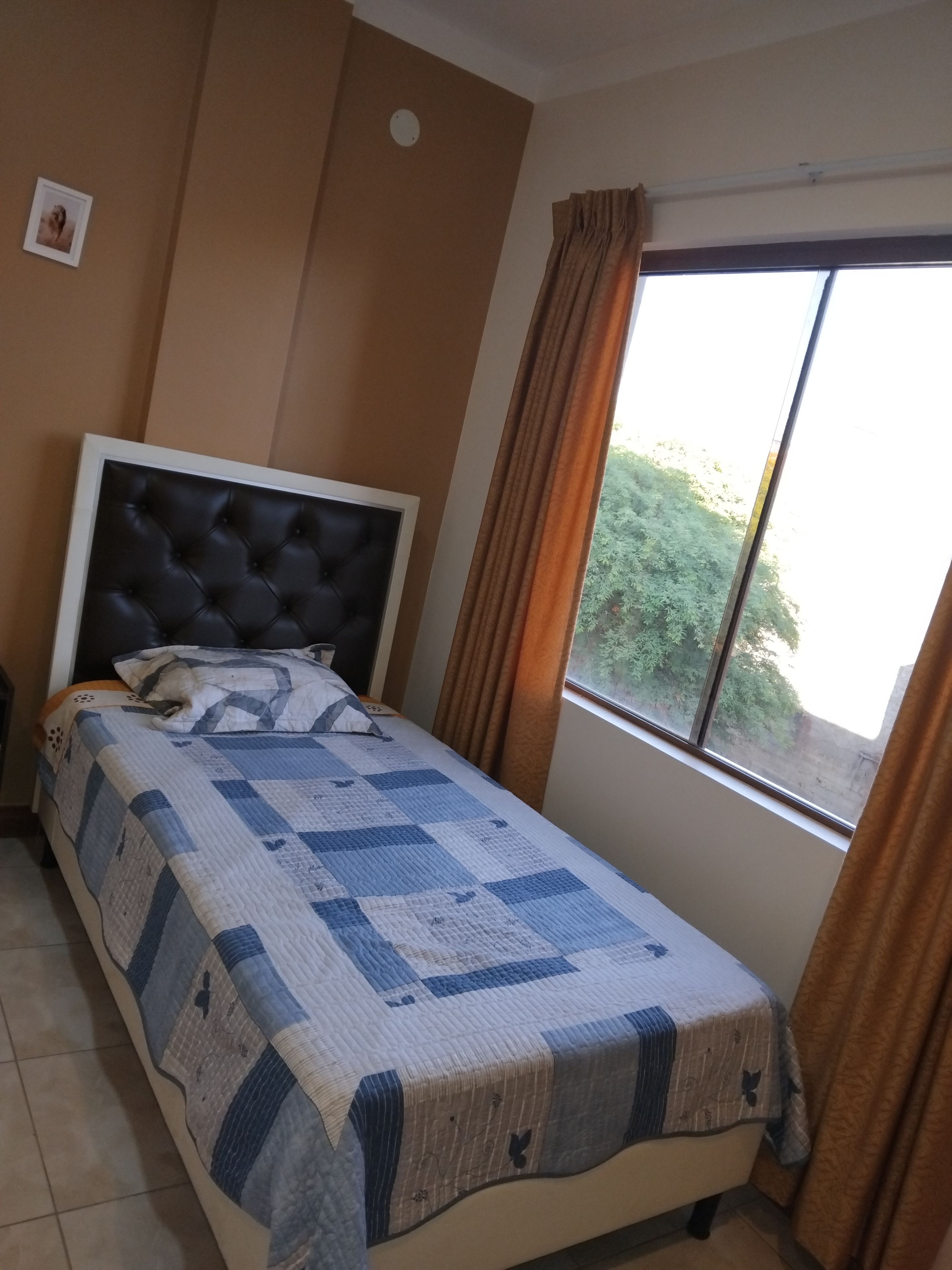 A bedroom with a bed, a window, and a wall-mounted light fixture.