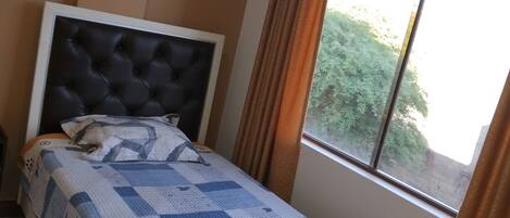A bedroom with a bed, a window, and a wall-mounted light fixture.