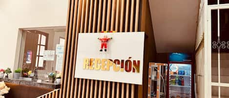 Zona de recepción con paneles de madera verticales, mostrador de recepción y máquina expendedora.