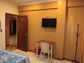Una habitación de hotel con cama, escritorio, televisor y perchero.