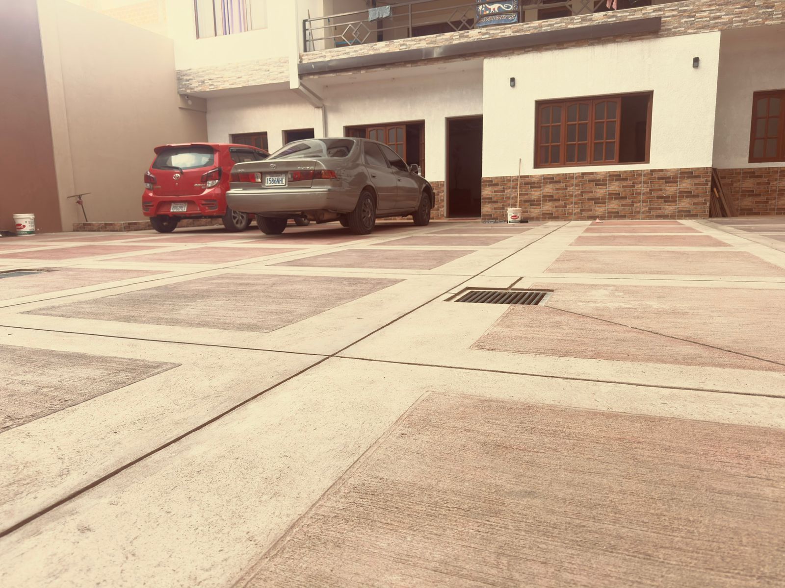 Un estacionamiento con dos autos, un SUV rojo y un sedán plateado, frente a un edificio con fachada de ladrillo y múltiples ventanas.