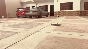 Un estacionamiento con dos autos, un SUV rojo y un sedán plateado, frente a un edificio con fachada de ladrillo y múltiples ventanas.