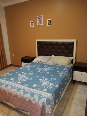 Une chambre à coucher avec un lit, deux tables de chevet et un mur orné de trois tableaux encadrés.