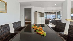 Un comedor moderno con una mesa de vidrio, sillas de mimbre y vista al mar a través de amplios ventanales.