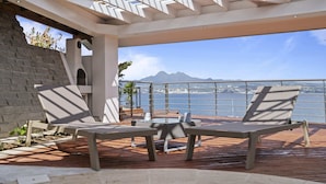 Una terraza con dos sillones de descanso y una mesa, con vista a un cuerpo de agua y una cordillera.