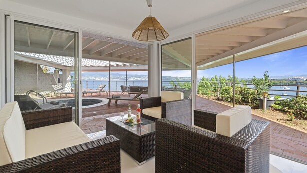 Un área de lounge exterior moderna con mobiliario de mimbre, una piscina cubierta de vidrio y vistas al mar.