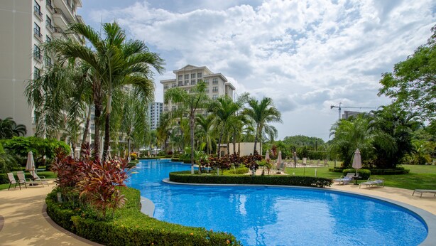 A swimming pool surrounded by palm trees and lounge chairs, with a large building in the background. - Jaco Bay 4303 (Jacó)
