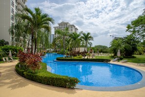 A swimming pool surrounded by palm trees and lounge chairs, with a large building in the background. - Jaco Bay 4303 (Jacó)