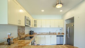 A modern kitchen with white cabinets, granite countertops, stainless steel appliances, and under-cabinet lighting. - Jaco Bay 4303 (Jacó)