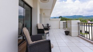 A balcony with wicker chairs and a table, a glass door, and a view of mountains. - Jaco Bay 4303 (Jacó)