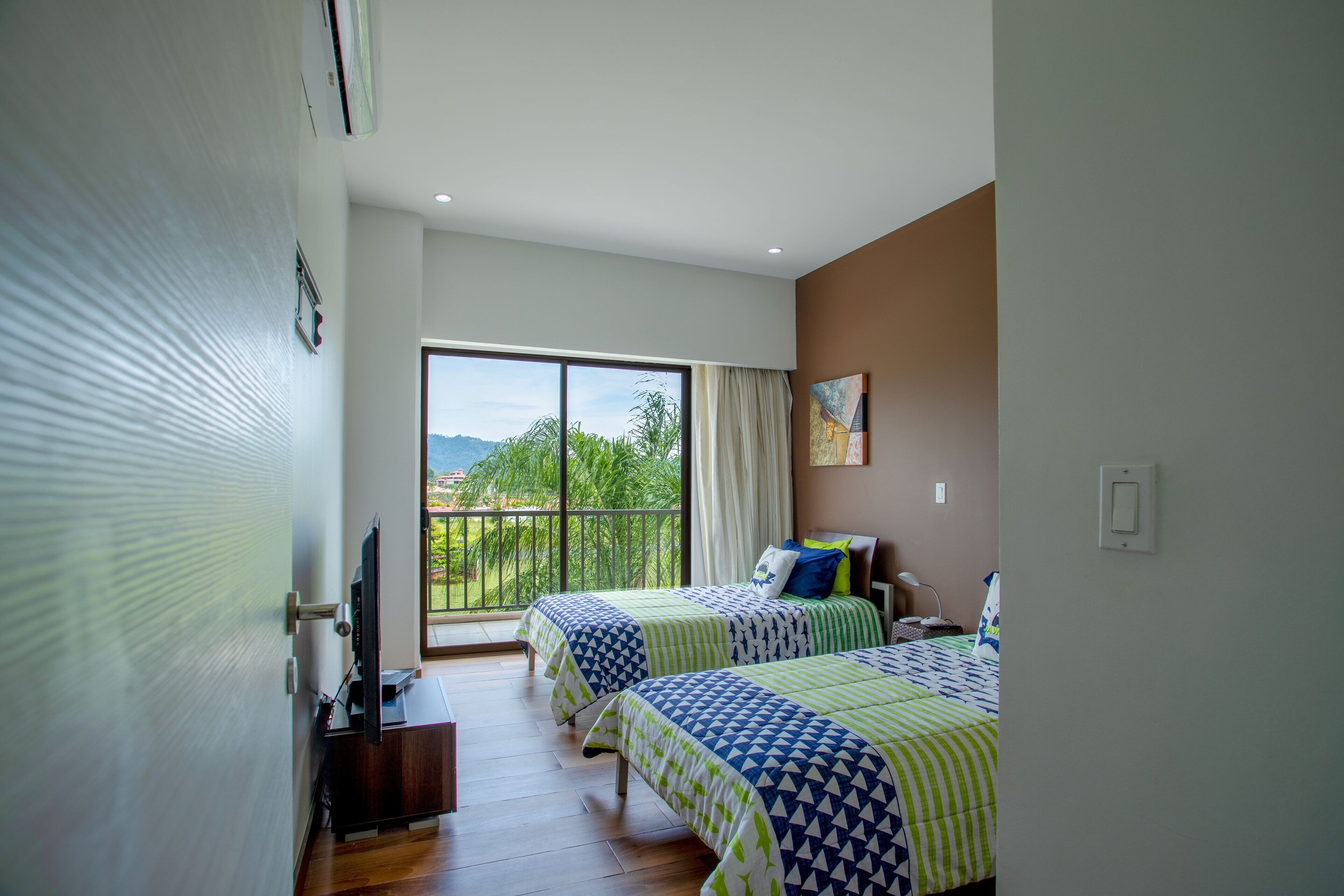 Habitación de hotel con dos camas, televisión y balcón con vistas.