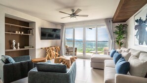 Ein modernes Wohnzimmer mit Sofa, Sesseln, Fernseher und großem Fenster mit Ausblick.