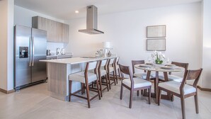 A modern kitchen with a stainless steel refrigerator, a built-in water dispenser, and a central island with bar stools. - Selva Coral 0701 (Jacó)