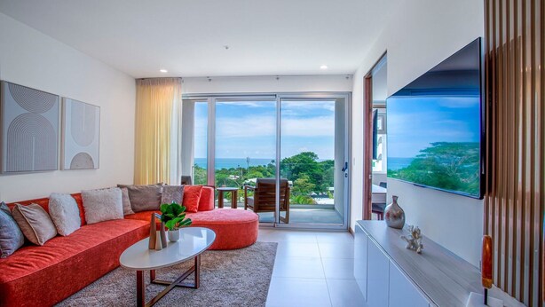 A modern living room with a red sofa, a coffee table, and a TV on a wall. - Selva Coral 0701 (Jacó)