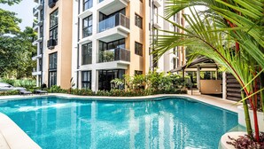 A modern hotel with a swimming pool, balconies, and lush greenery. - Torres del Mar 1202 (Jacó)