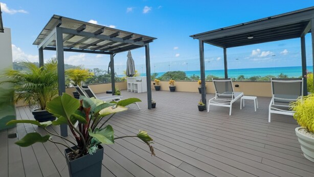 A rooftop terrace with a pergola, lounge chairs, potted plants, and a view of the ocean. - Torres del Mar 1202 (Jacó)