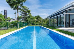 A rectangular swimming pool with clear blue water, surrounded by a grassy area and a glass-enclosed building. - Viva Jaco Viva Jaco (Jacó)