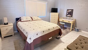 Ein Schlafzimmer mit Bett, Schreibtisch, Stuhl, Kommode und Deckenventilator.