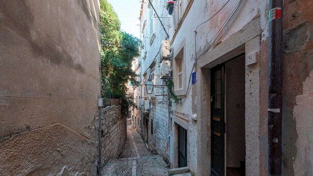 Une ruelle étroite entre deux bâtiments, avec une porte et une fenêtre visibles.