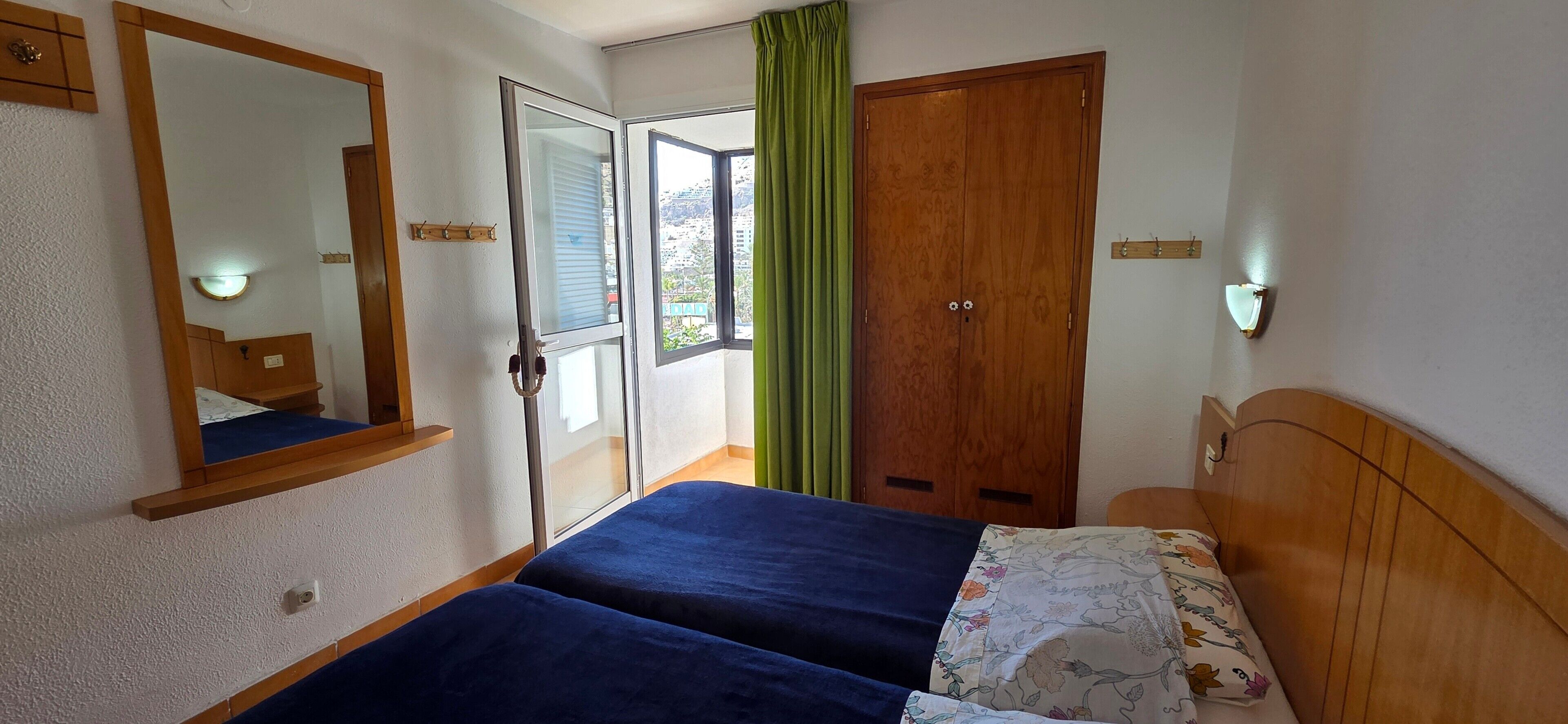 Un dormitorio con dos camas, un armario de madera, un espejo y una ventana con cortinas.