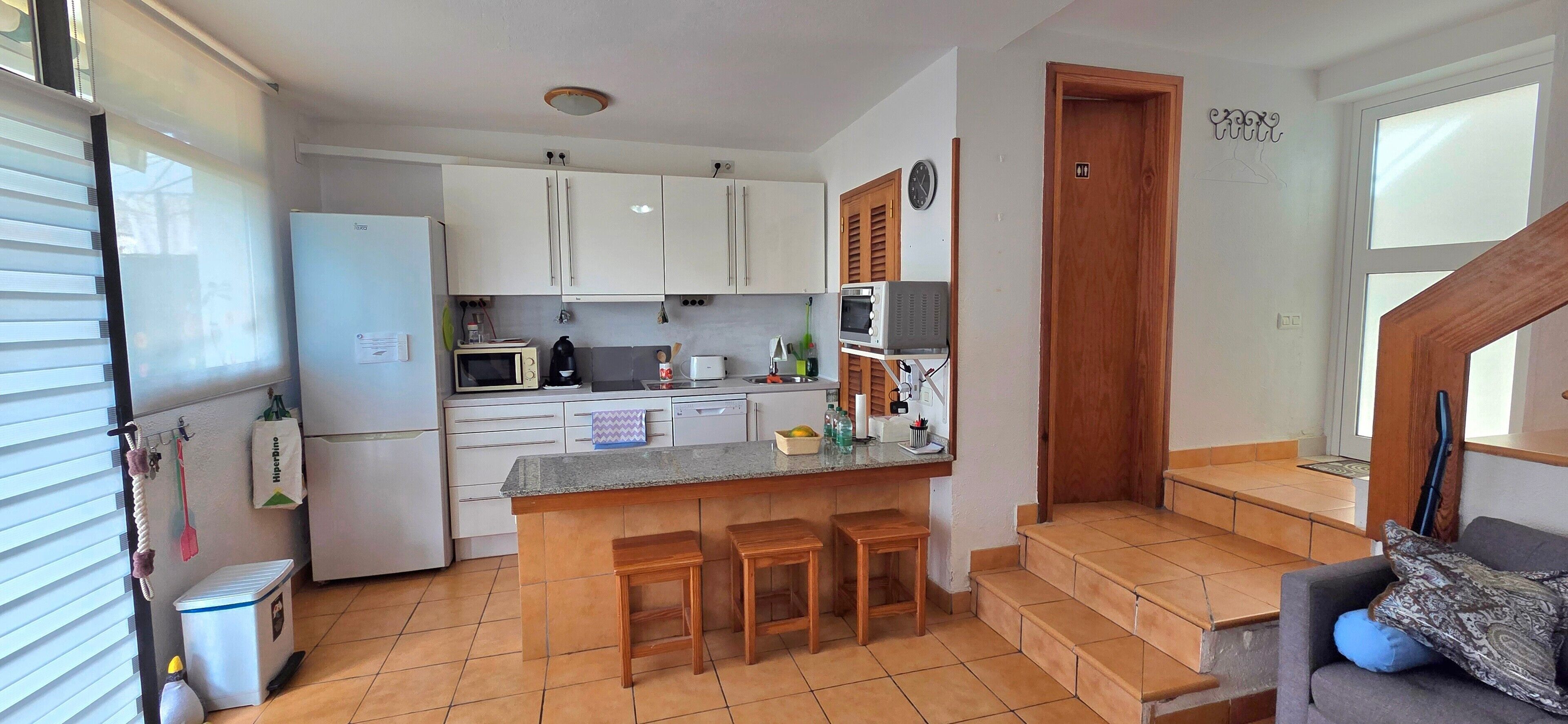 Una cocina compacta con refrigerador, microondas y una pequeña isla con taburetes.