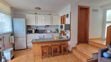 Una cocina compacta con refrigerador, microondas y una pequeña isla con taburetes.