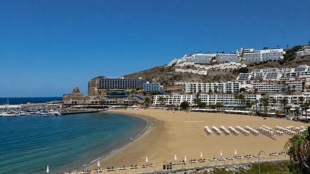 Un hôtel situé sur la côte, composé de plusieurs bâtiments, avec une plage équipée de transats et une marina où sont amarrés des bateaux.