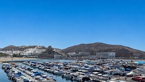 Un port de plaisance où sont amarrés de nombreux bateaux, un ciel dégagé et un paysage montagneux en toile de fond.