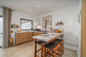 A modern kitchen with a central island, wooden stools, a built-in oven, and a window with a view.