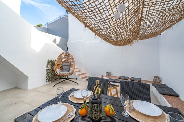 A dining area with a table set for two, a wicker chair, and a cushioned bench.