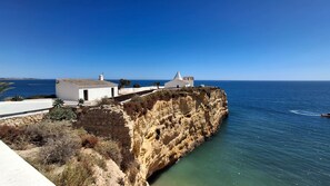 A coastal building with a stone facade, white walls, and a clear view of the sea. - Algarve house with patio & terrace, 2 bedrooms, near beaches, fully renovated (Parchal)