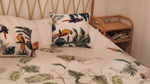 Una cama con colcha de estampado de aves tropicales, un espejo de pared circular y un cabecero de ratán.