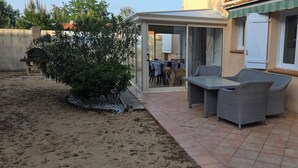 Um alpendre coberto com mesa e cadeiras, um pequeno jardim e vista para a casa.