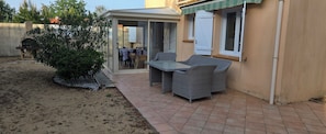 Une terrasse couverte avec une table et des chaises, un petit jardin et une vue sur l’intérieur de la maison.
