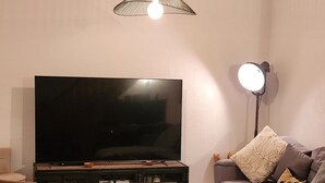 A living room with a large wall clock, a television, a sofa, a coffee table, and a hanging light fixture.