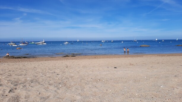 Una playa con barcos en el agua y gente en la orilla.