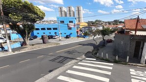 Vista da rua com um edifício azul, uma faixa de pedestres e um carro vermelho estacionado na lateral.