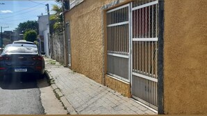 Uma rua estreita com um carro estacionado e um prédio com janelas protegidas por grades.