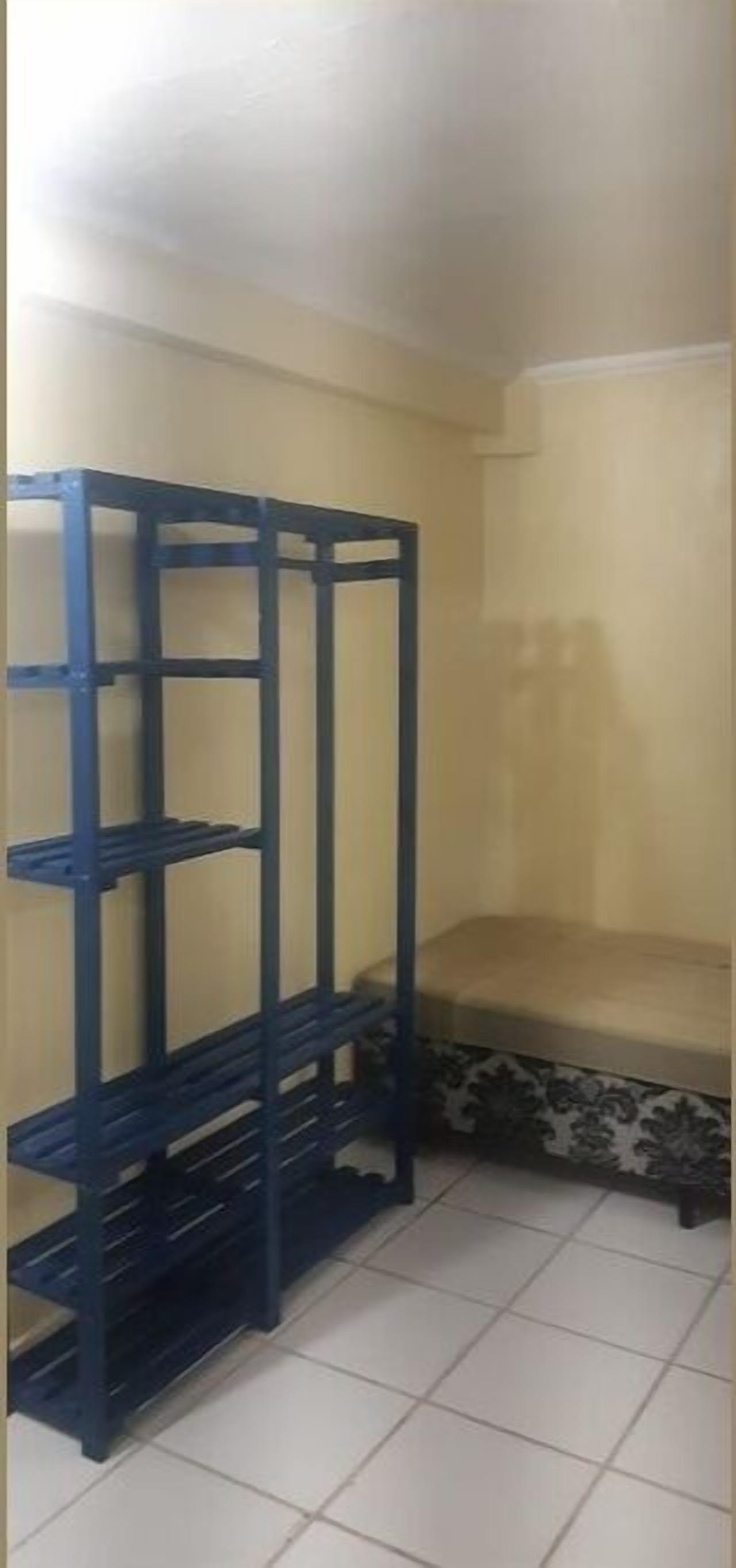 A corner room with a blue metal shelf unit against the wall and a bench with a patterned cushion.