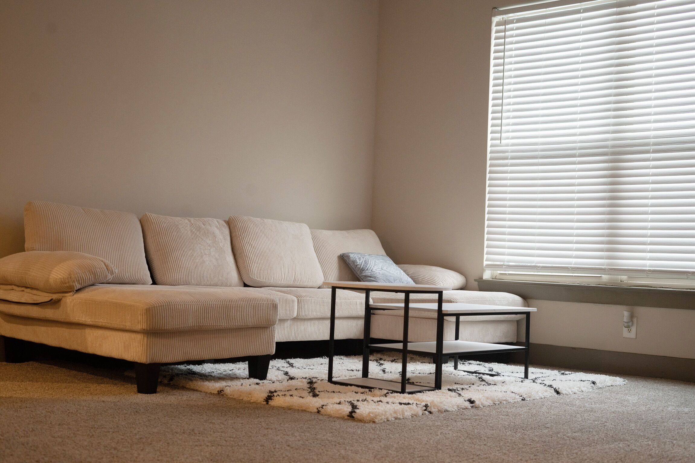A beige sofa with multiple cushions, a small black coffee table, and a patterned rug.