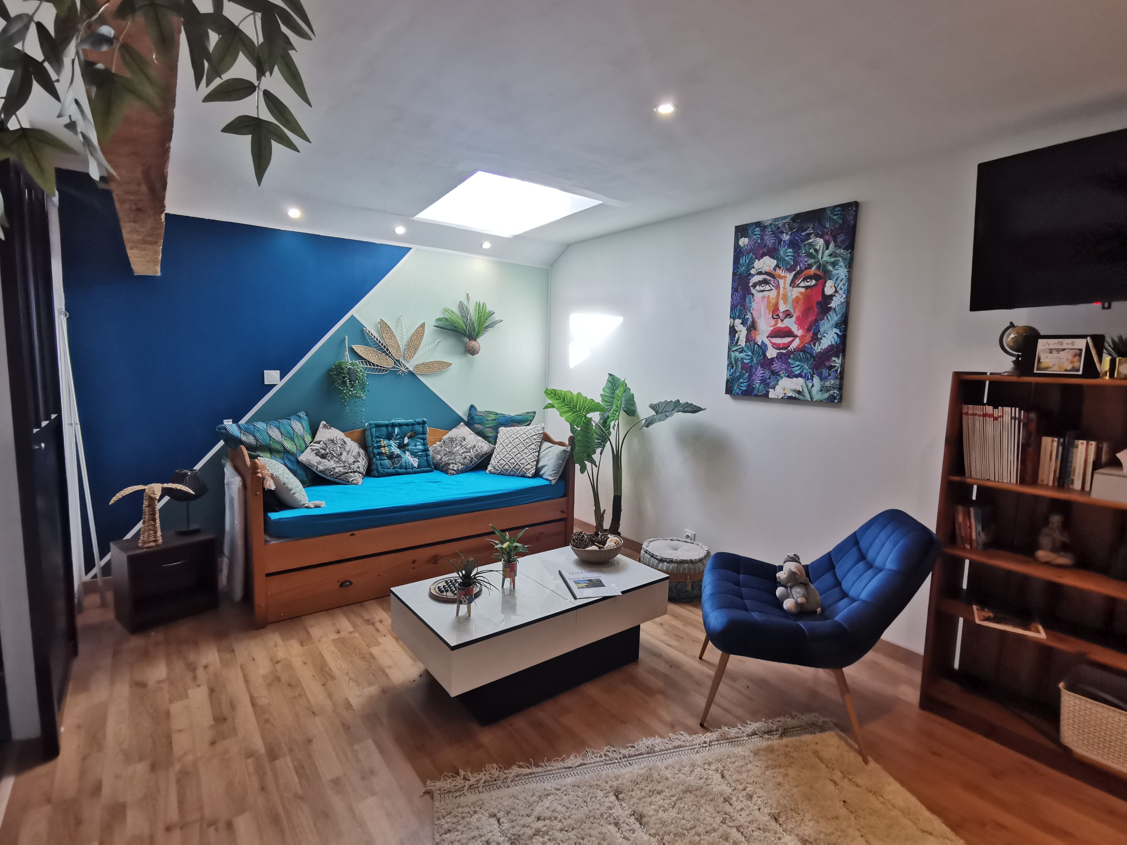 Un salon moderne avec un mur d’accent bleu, un canapé, une table basse, un fauteuil bleu et une bibliothèque.