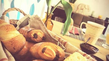 A basket of assorted pastries and bread, a vase with a plant, and a coffee cup on a table.