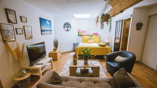 A living room with a sofa, a TV, a coffee table, and a bed with yellow bedding. - La Grange de Cablanc (Monestier)