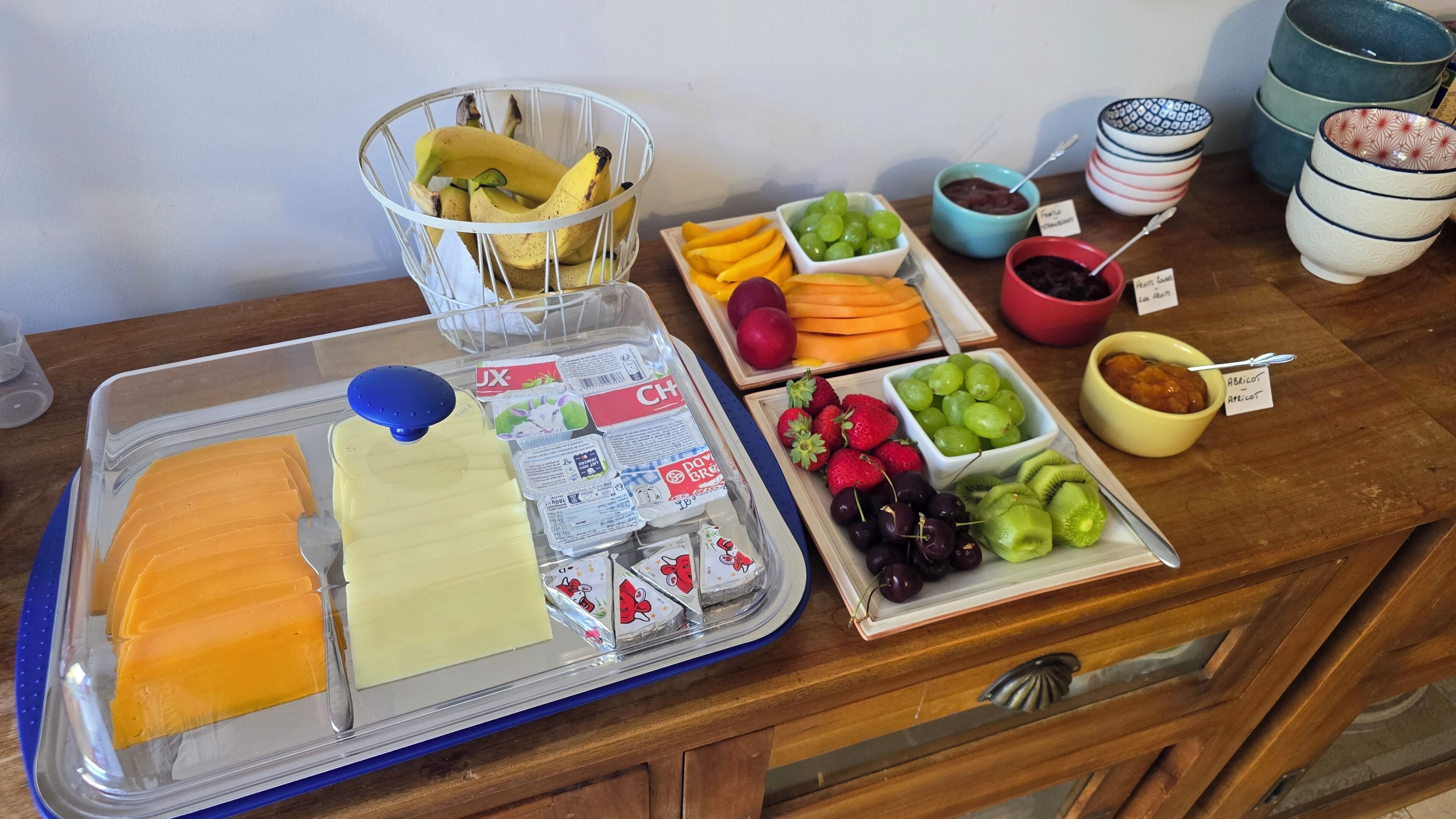 Une table de buffet proposant une variété d’aliments, notamment des fruits, des fromages et des condiments.