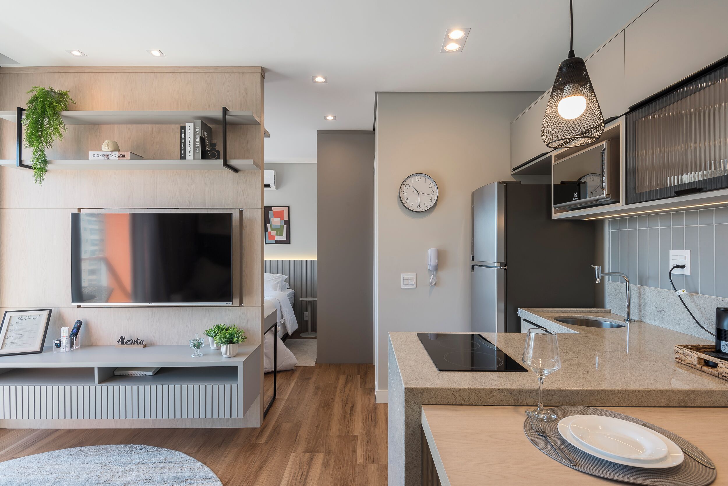 A modern living room with a flat-screen TV, a built-in bookshelf, and a dining area with a glass-top table and a wine glass.